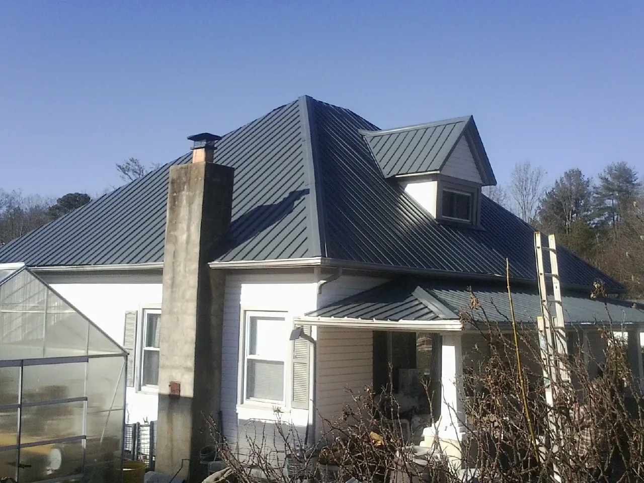 Dark blue standing seam metal roof on a white farmhouse with dormer — Slate & Tile Roof Repair by Roofing Brothers in Cicero