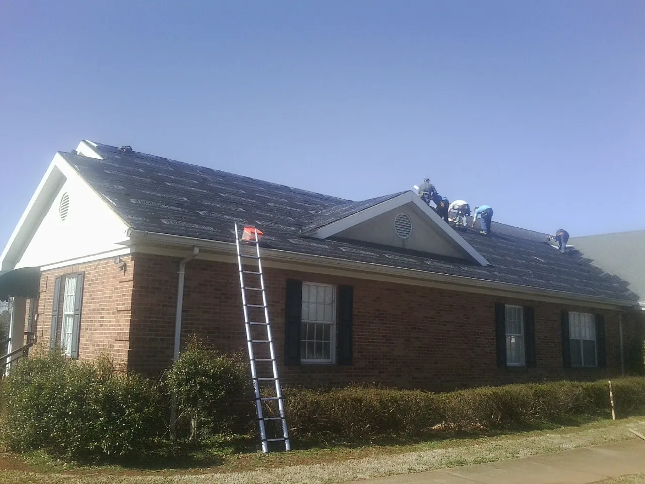 Crew tearing shingles off a brick ranch roof with a ladder set — Emergency Roof Repair work by our crew in Cicero