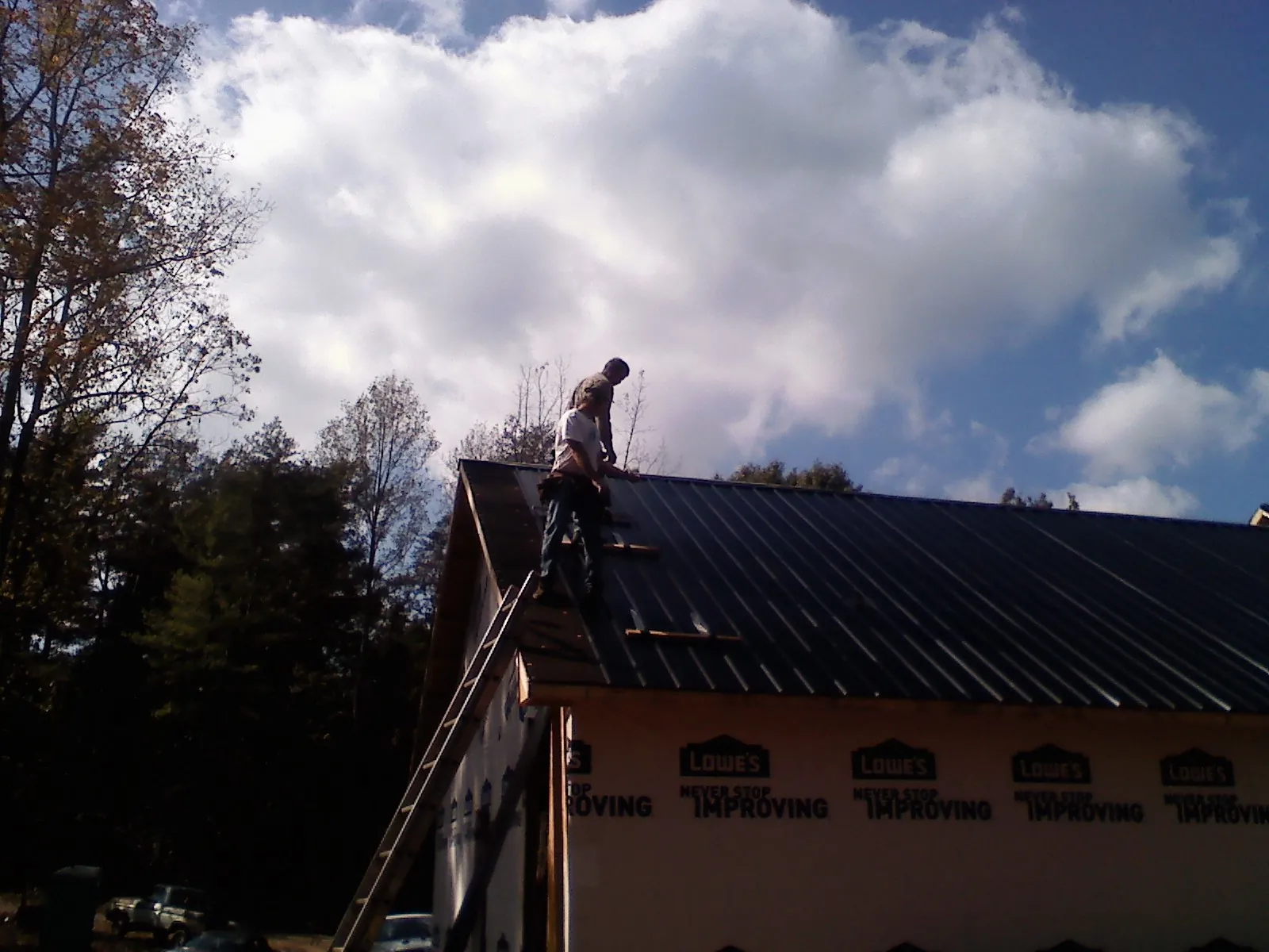 Roofer fastening dark metal panels high against a cloudy sky, from a Roof Inspection job in Cicero